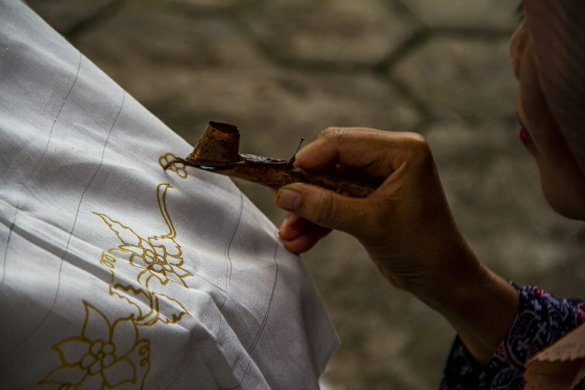 Artisan drawing a batik pattern in wax with a canting