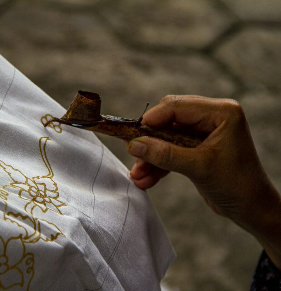 Artisan drawing a batik pattern in wax with a canting